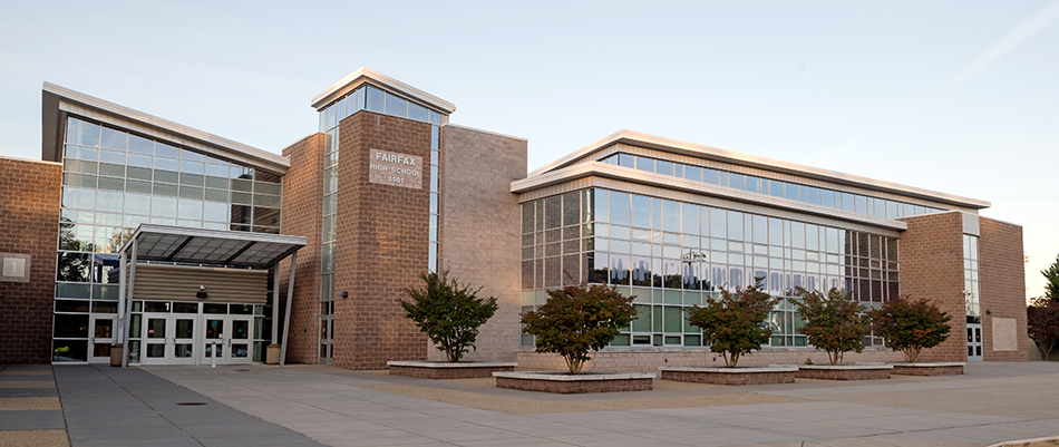 Entryway of the newly renovated Fairfax High School. The building has a very modern look with angled roof sections and large glass windows running the length of the front. The photograph was taken shortly after sunrise and there is a pink glow on the windows.