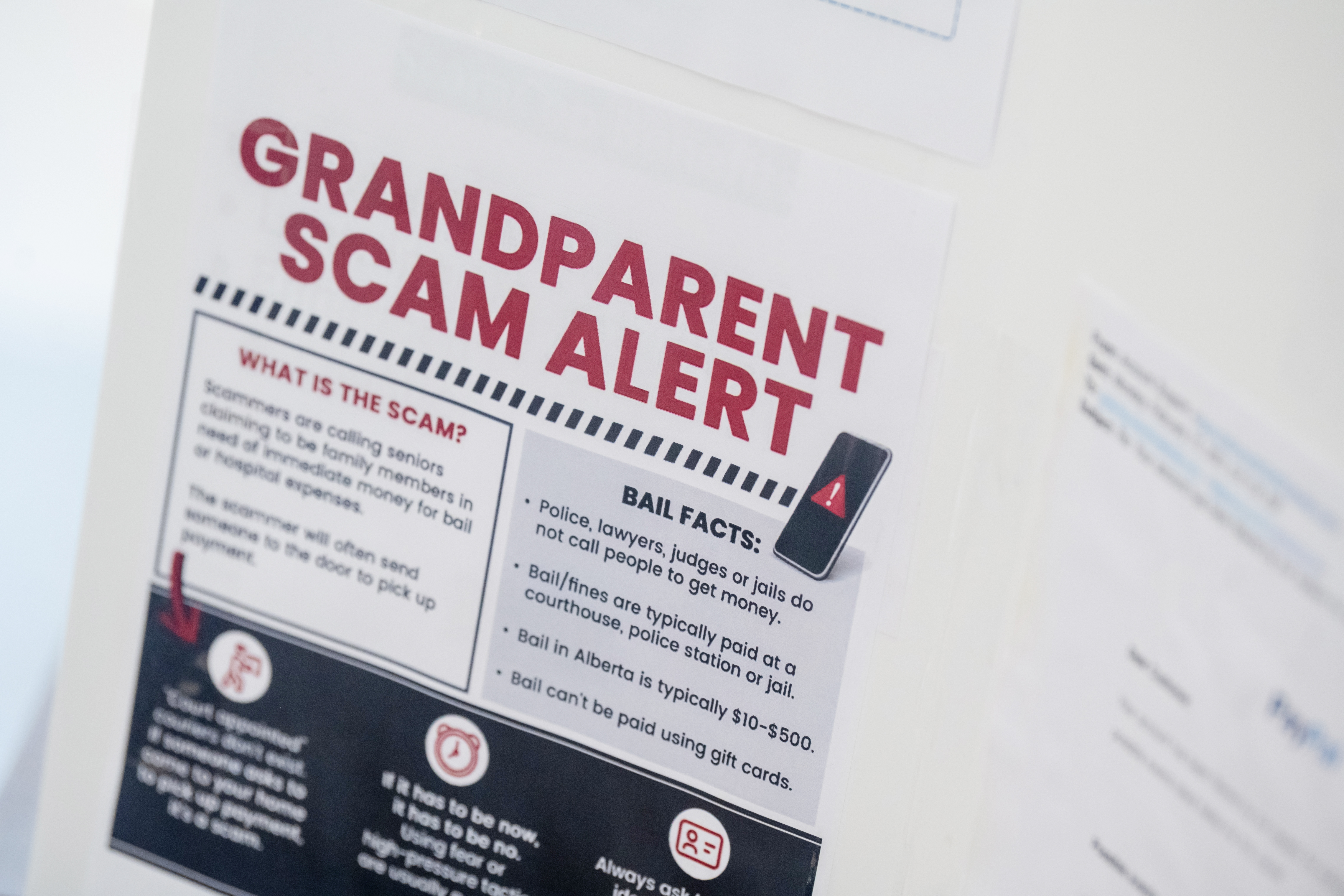 The camera focuses on a card glued to a poster board. The card reads, in large red capital letters, "GRANDPARENT SCAM ALERT." Text in boxes below the title explain what the scam is.t